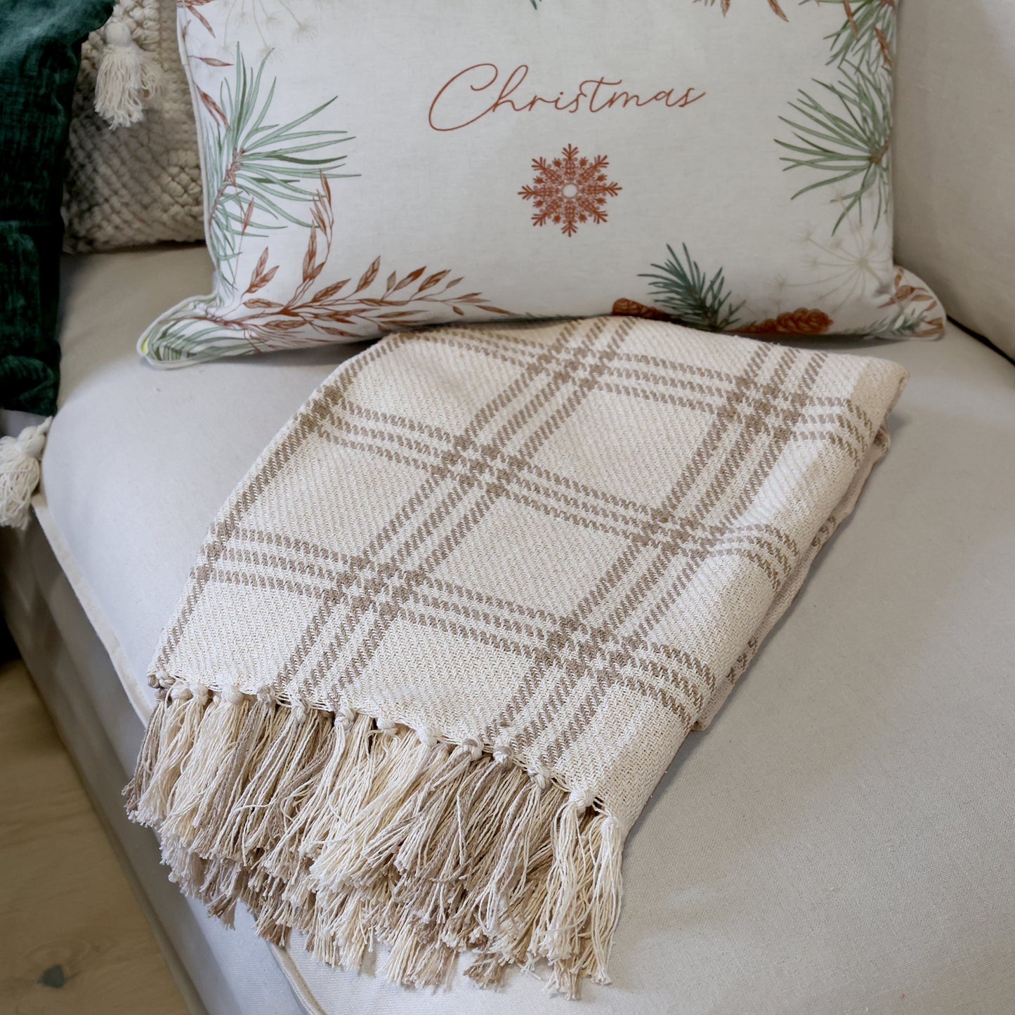 Plaid blanket with fringe on a sofa with Christmas-themed pillow
