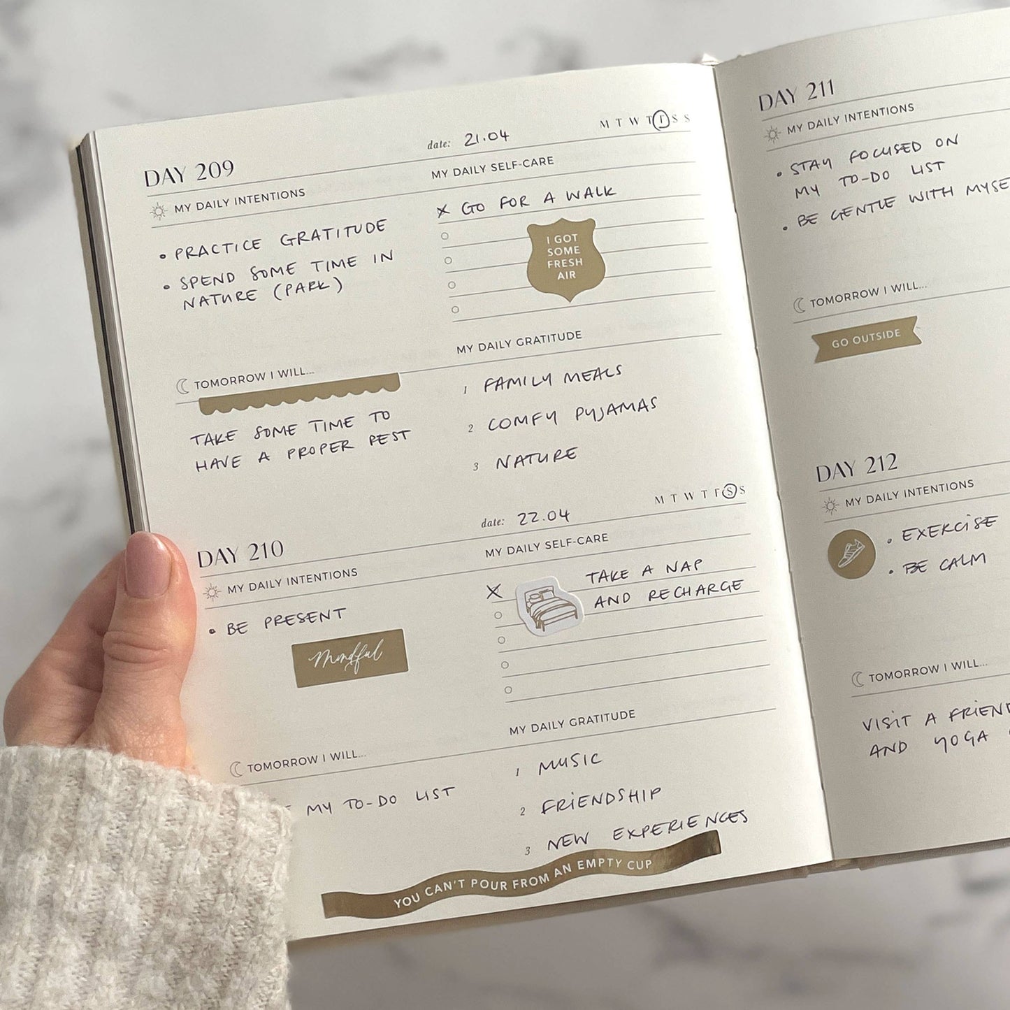 Hand holding a planner with daily intentions and tasks on a light background