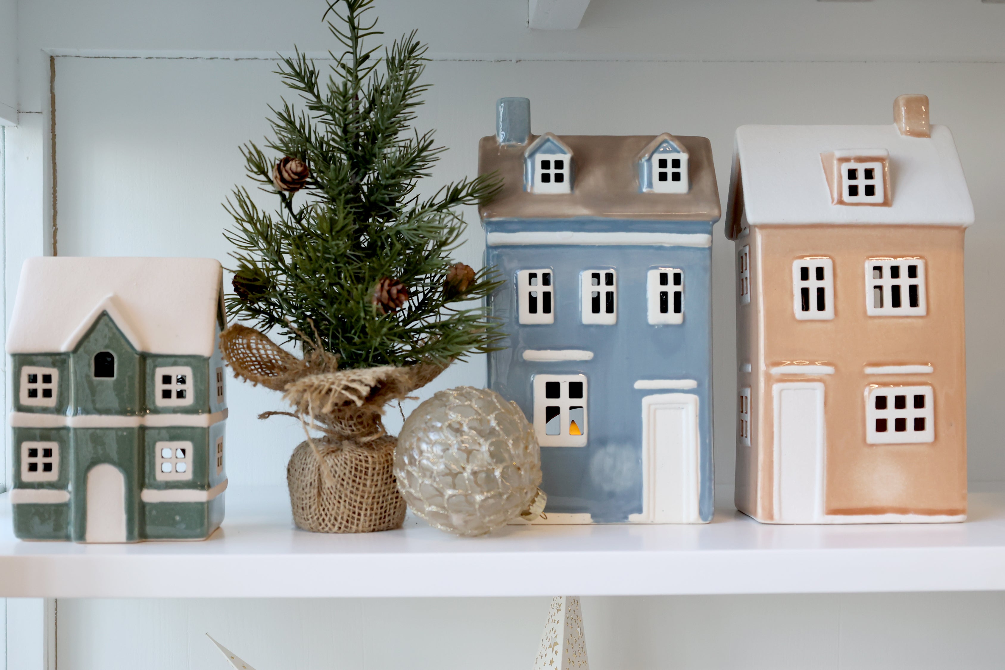 Decorative ceramic houses on a shelf with a small tree and ornaments.