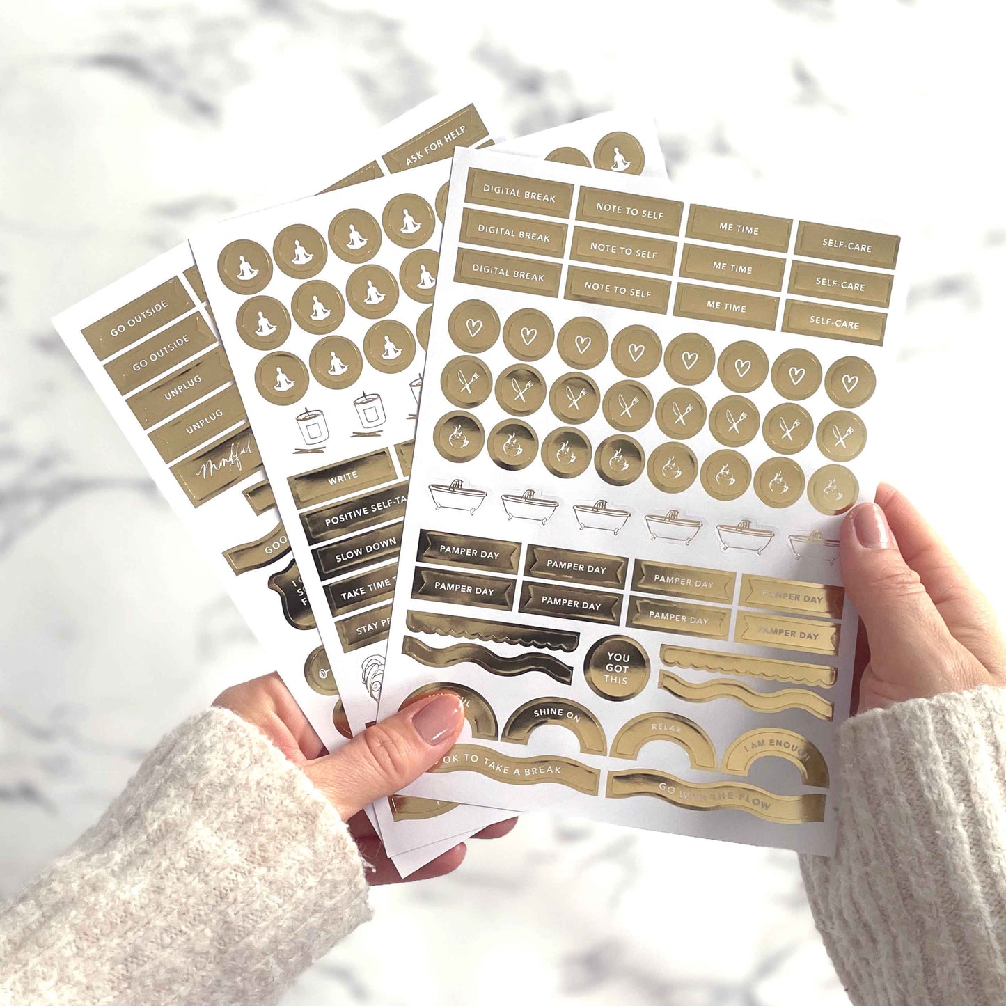 Set of gold planner stickers held by a person against a blurred background