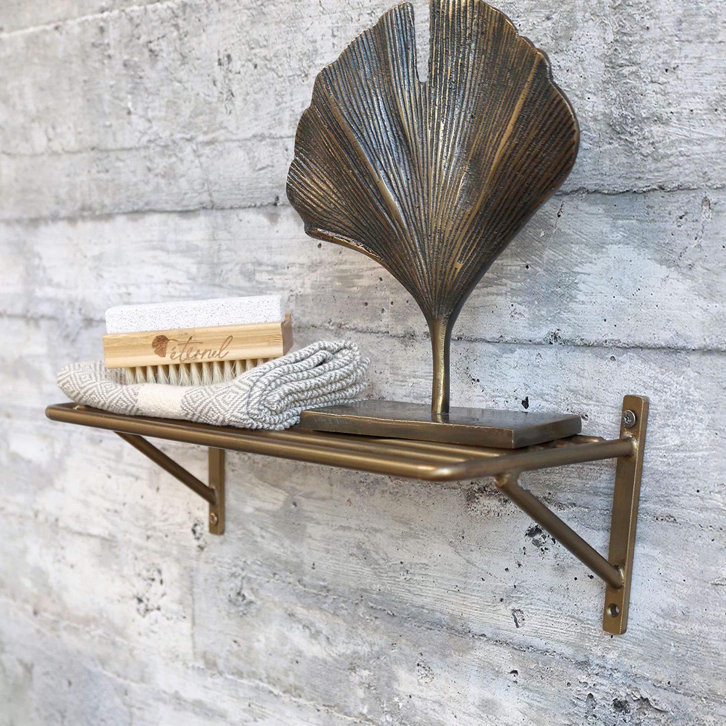 Brass wall shelf with decorative leaf design against a textured wall.