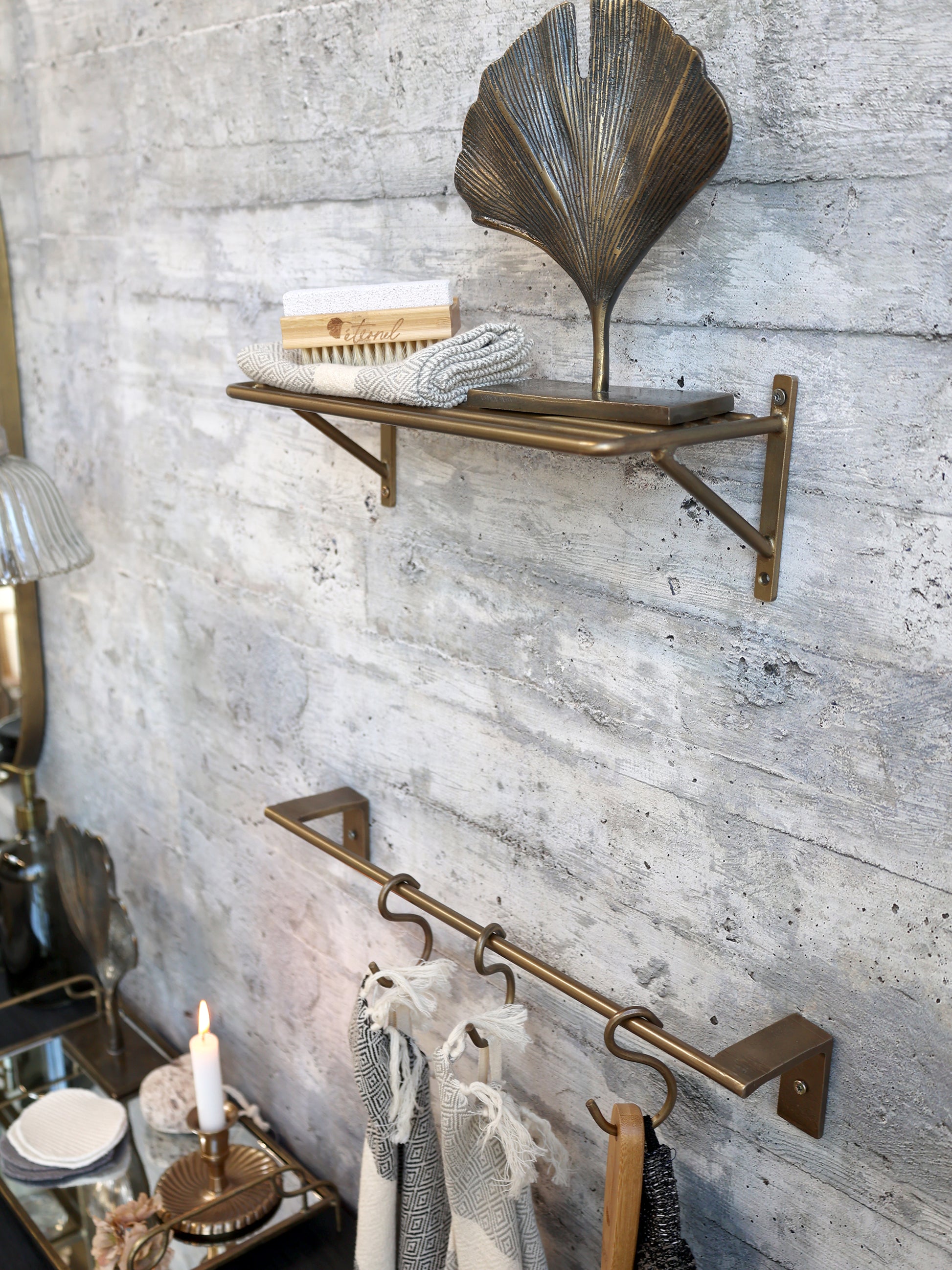 Brass wall shelf and bar mounted on a textured gray wall with decorative items.