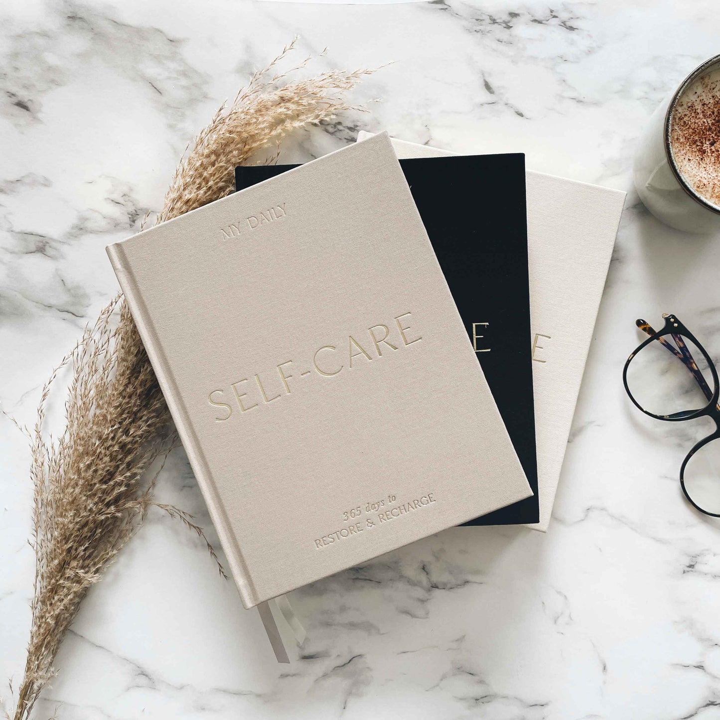 Notebook titled 'Self-Care' on a marble surface with a cup of coffee and glasses.