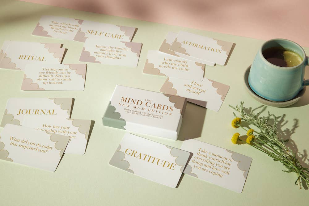 Set of self-care mind cards on a table with a cup of tea and flowers.