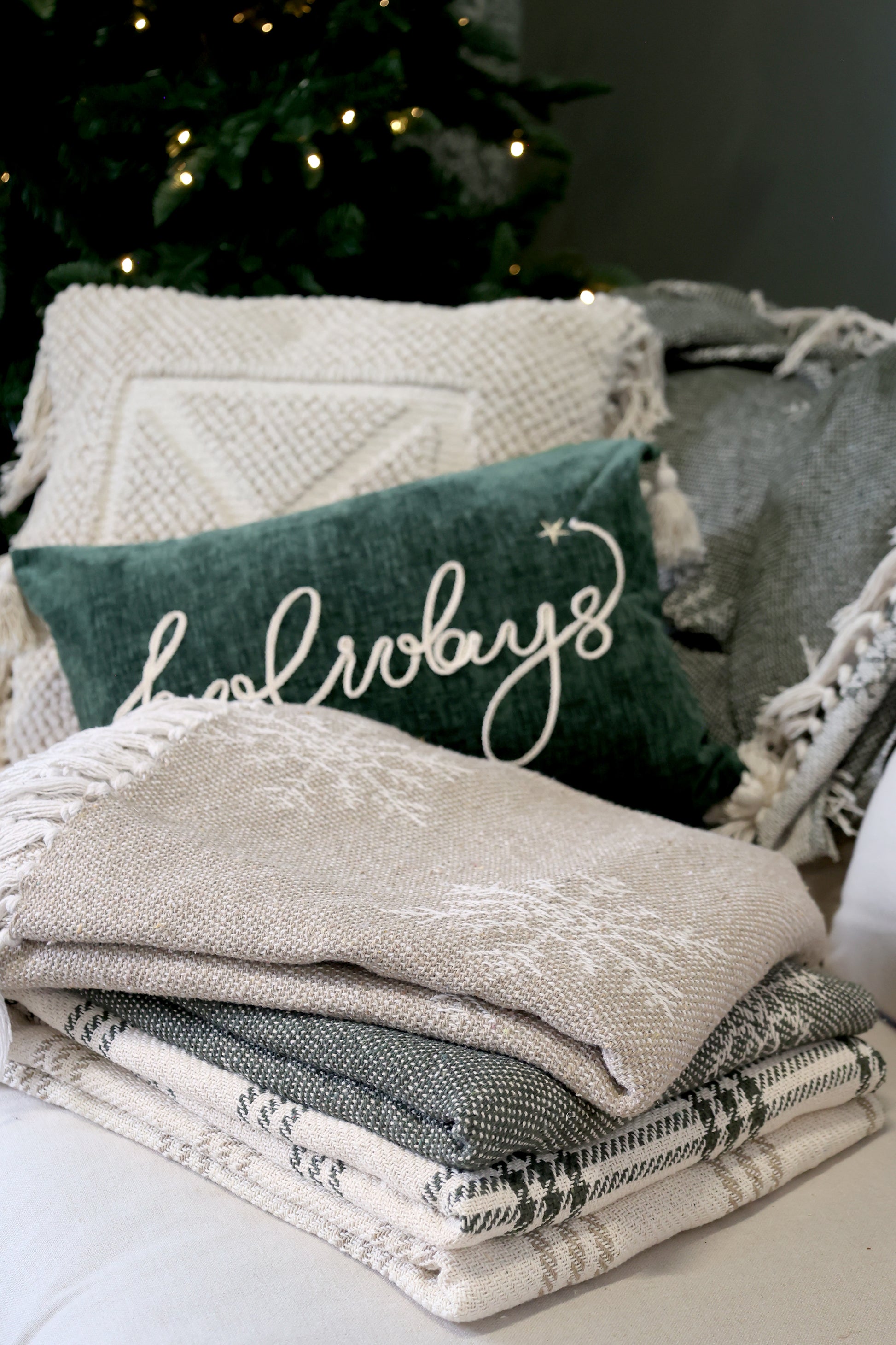 Stack of textured blankets with a decorative pillow featuring the word 'forever' in a cozy indoor setting.