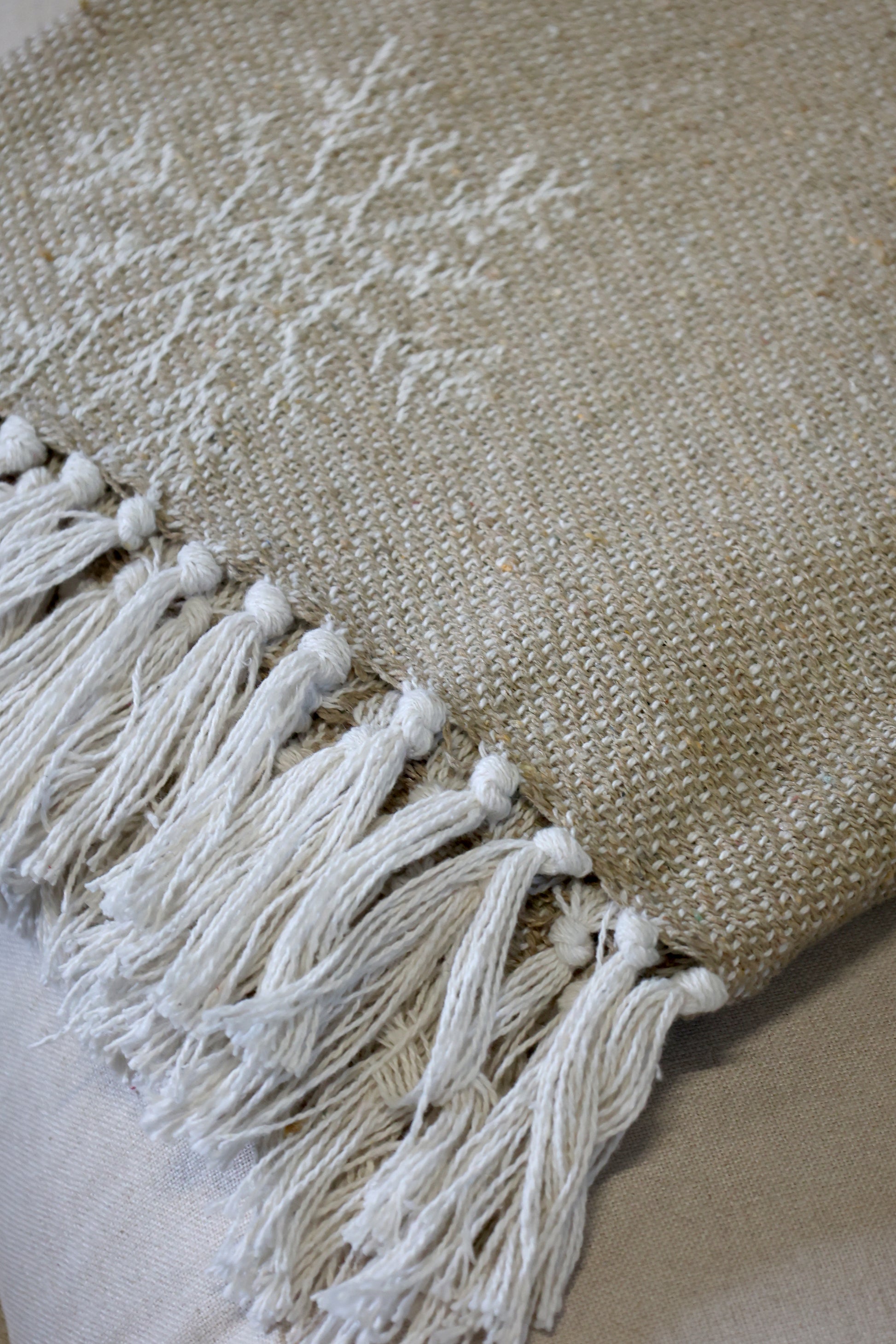 Textured beige throw with white tassels on a neutral background