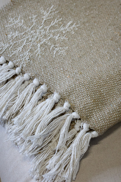 Textured beige throw with white tassels on a neutral background
