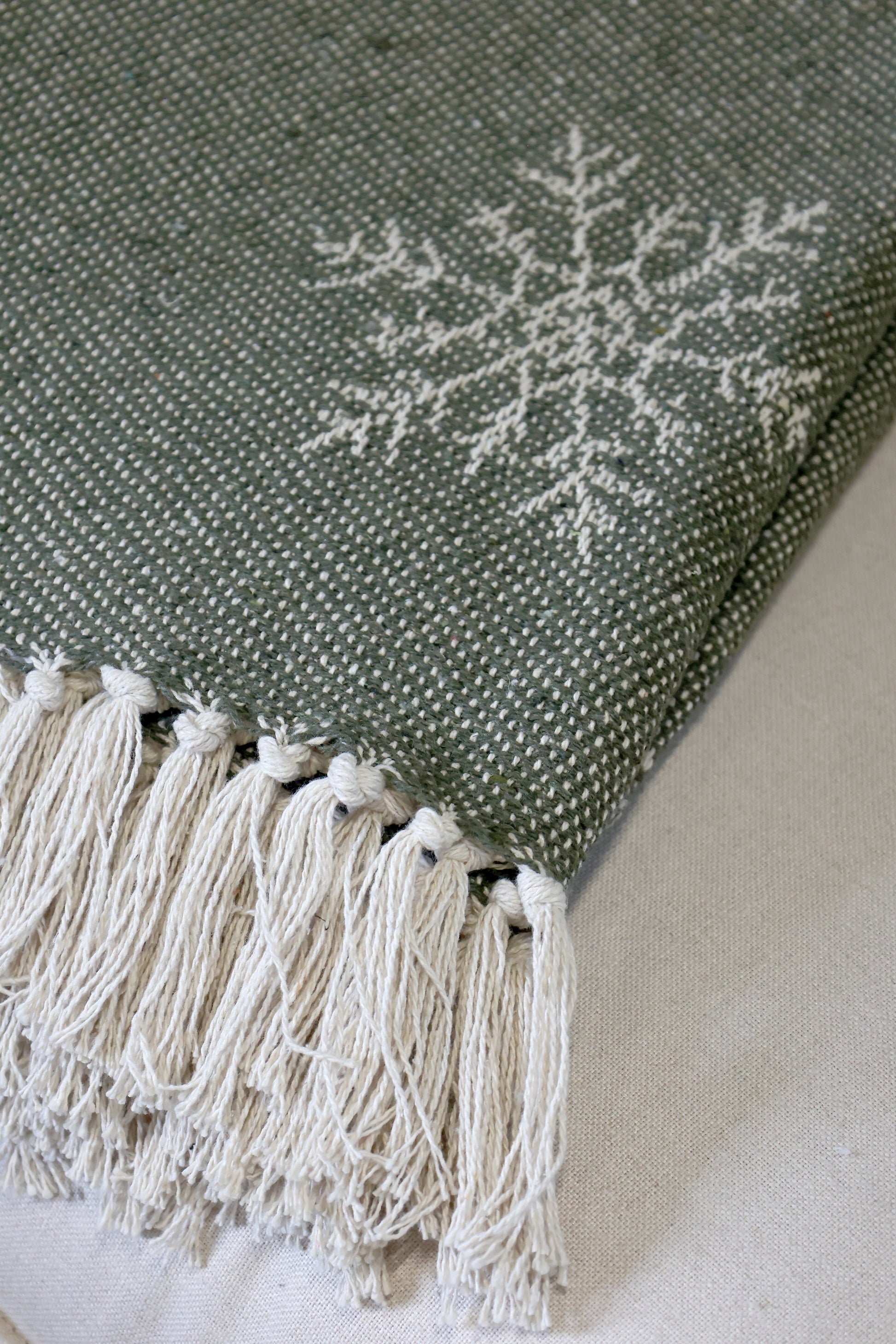 Green textured fabric with white embroidered design and tassels on a light background