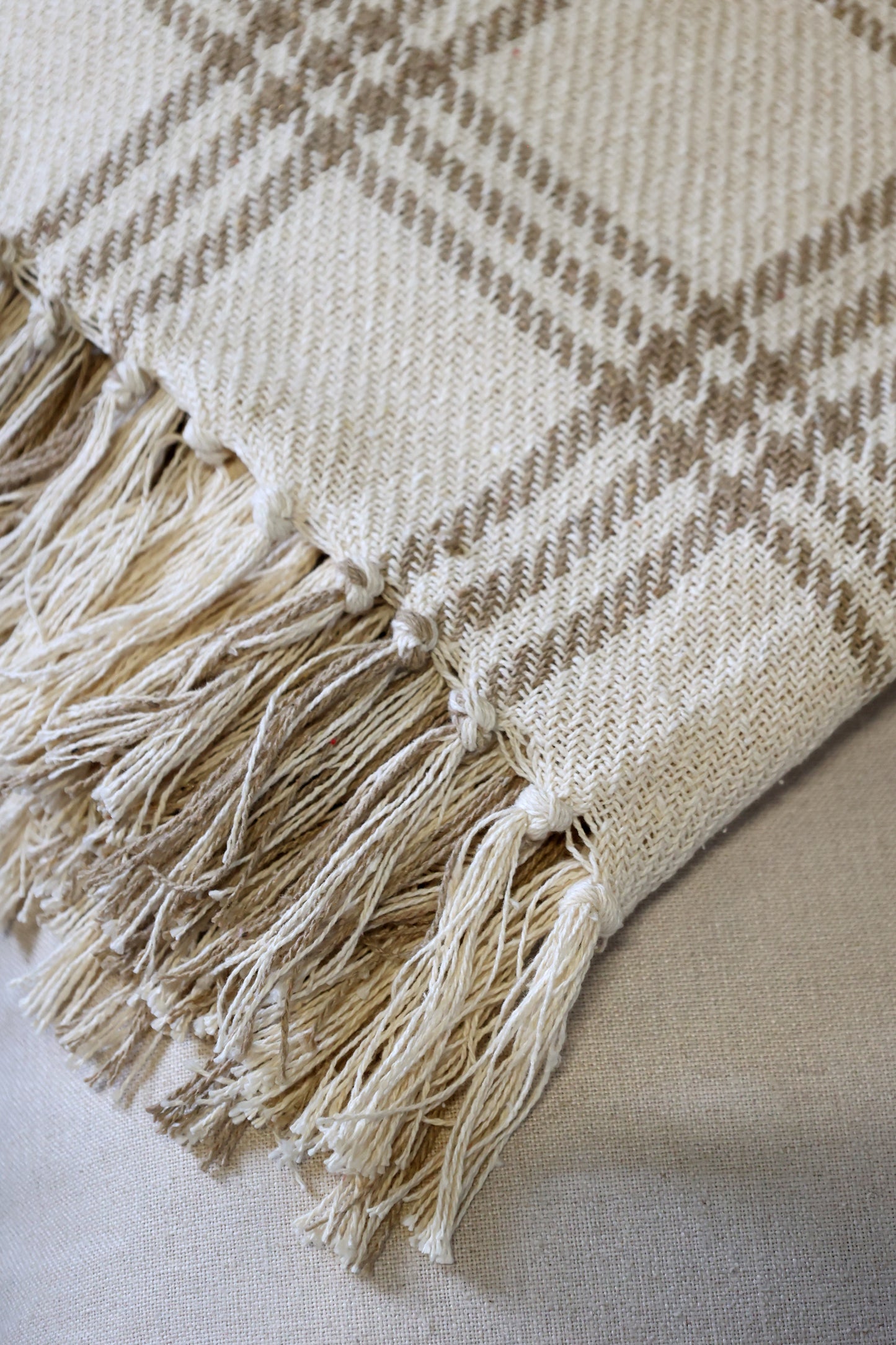 Beige and brown plaid blanket with tassels on a light background