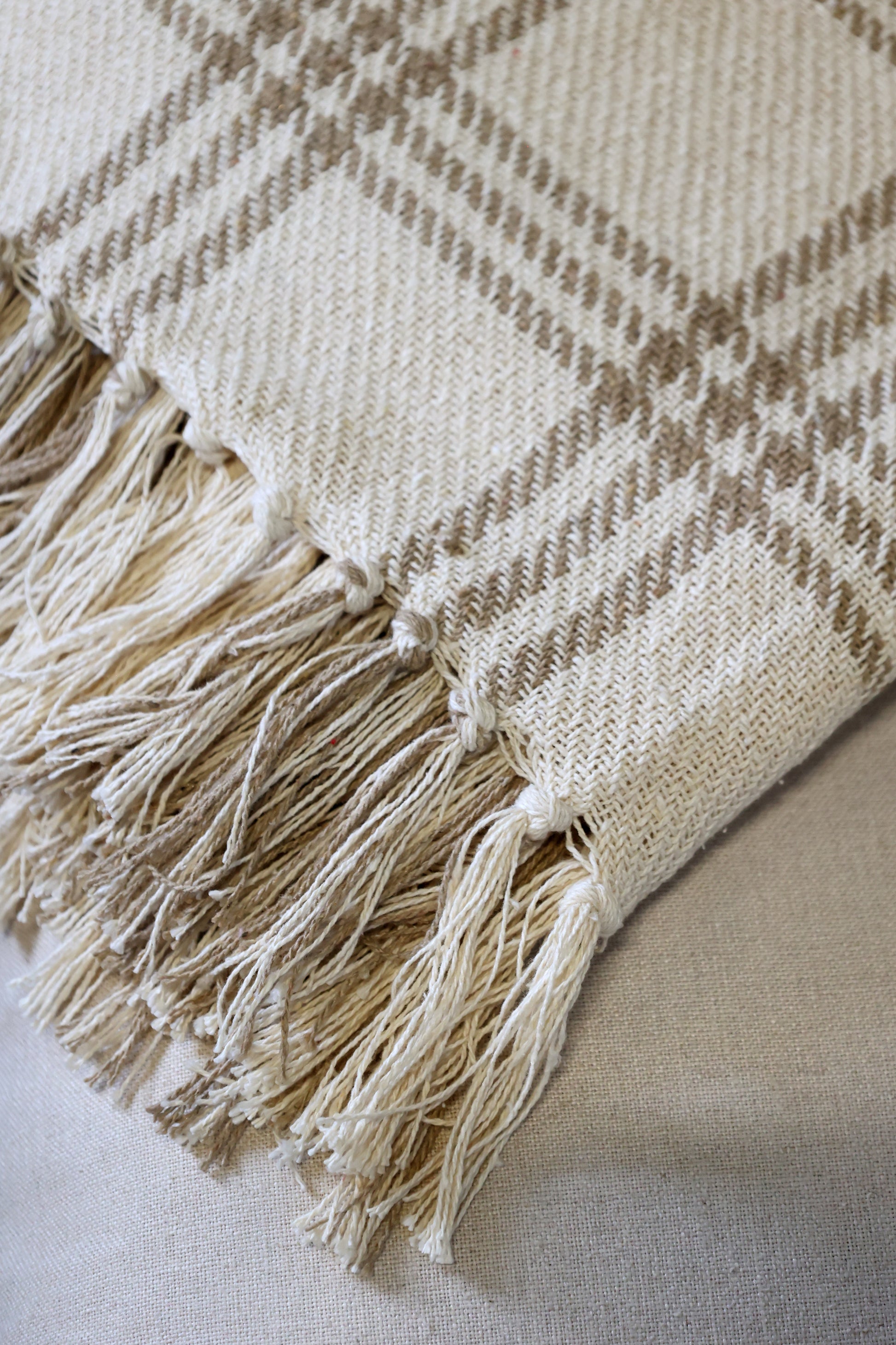 Beige and brown plaid blanket with tassels on a light background