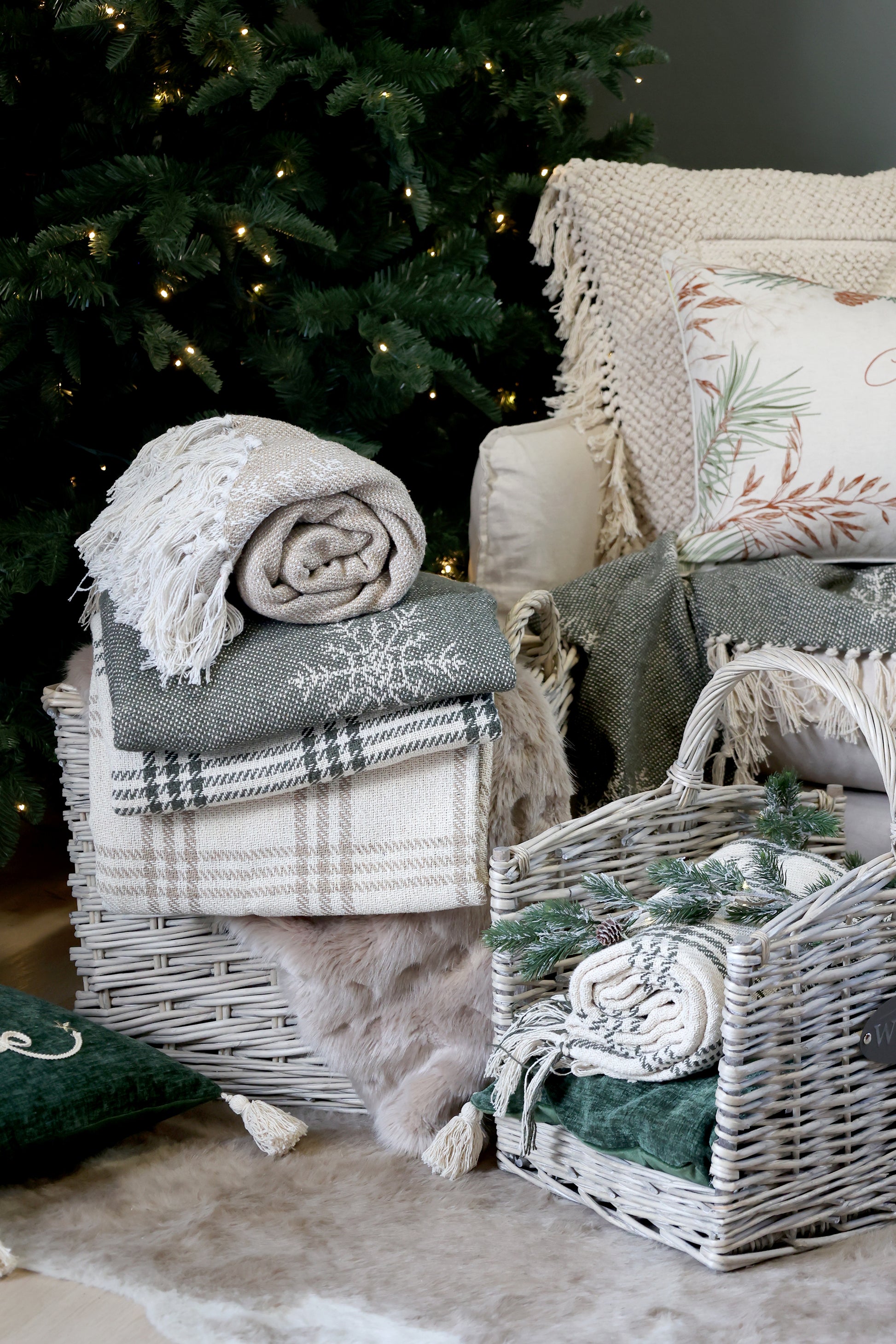 Decorative scene with plaid blanket, textured pillows, and wicker basket against a Christmas tree.