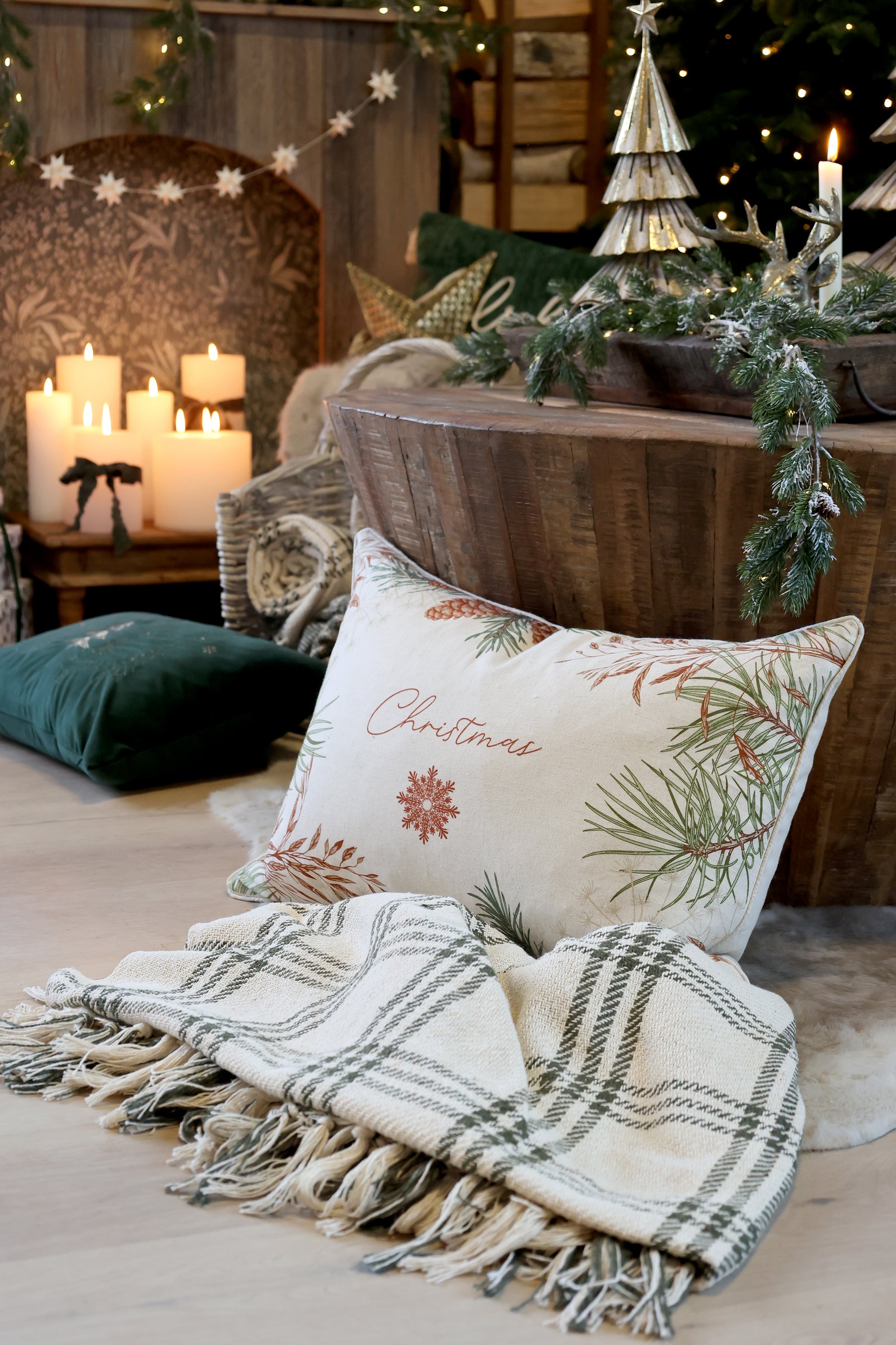Decorative Christmas pillow with festive design on a bed with a blanket and candles.