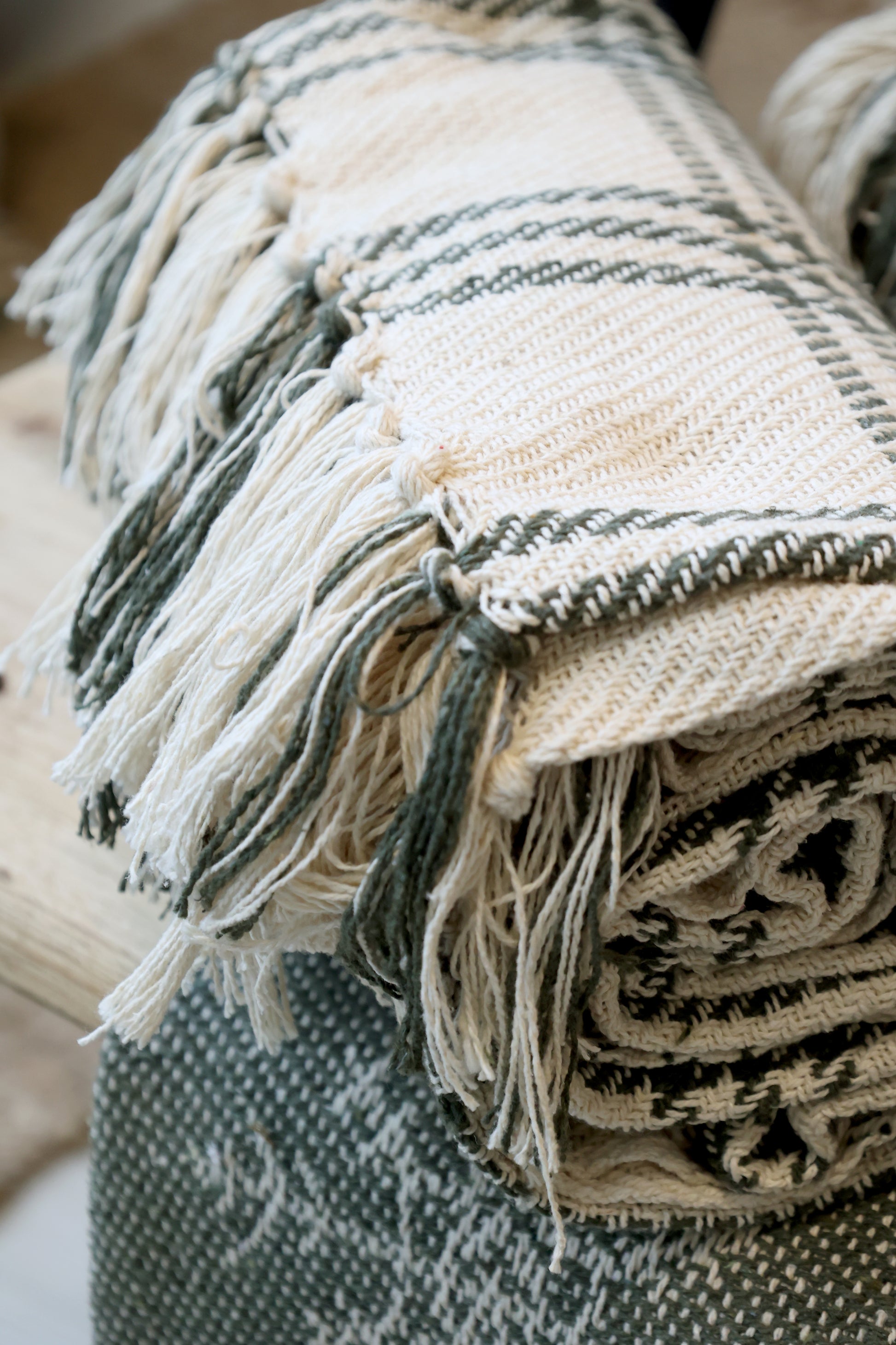 Stack of woven blankets with fringes on a neutral background