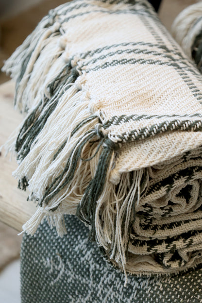 Stack of woven blankets with fringes on a neutral background