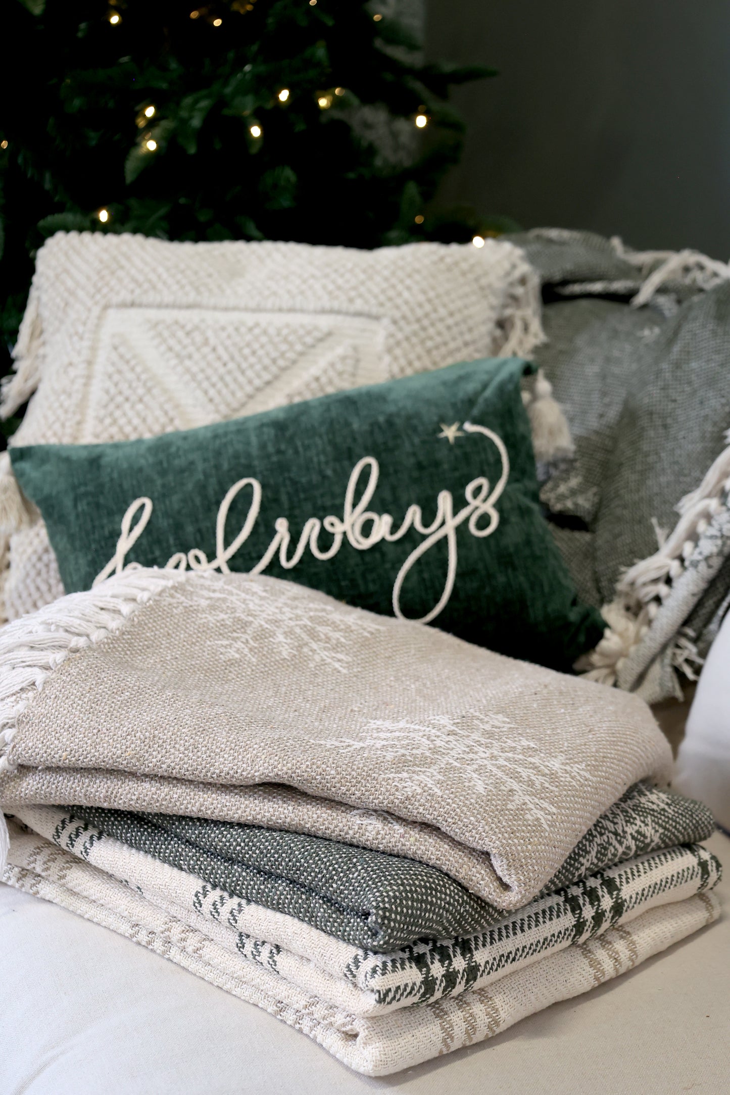 Stack of textured blankets with a decorative pillow featuring the word 'forever' in a cozy indoor setting.