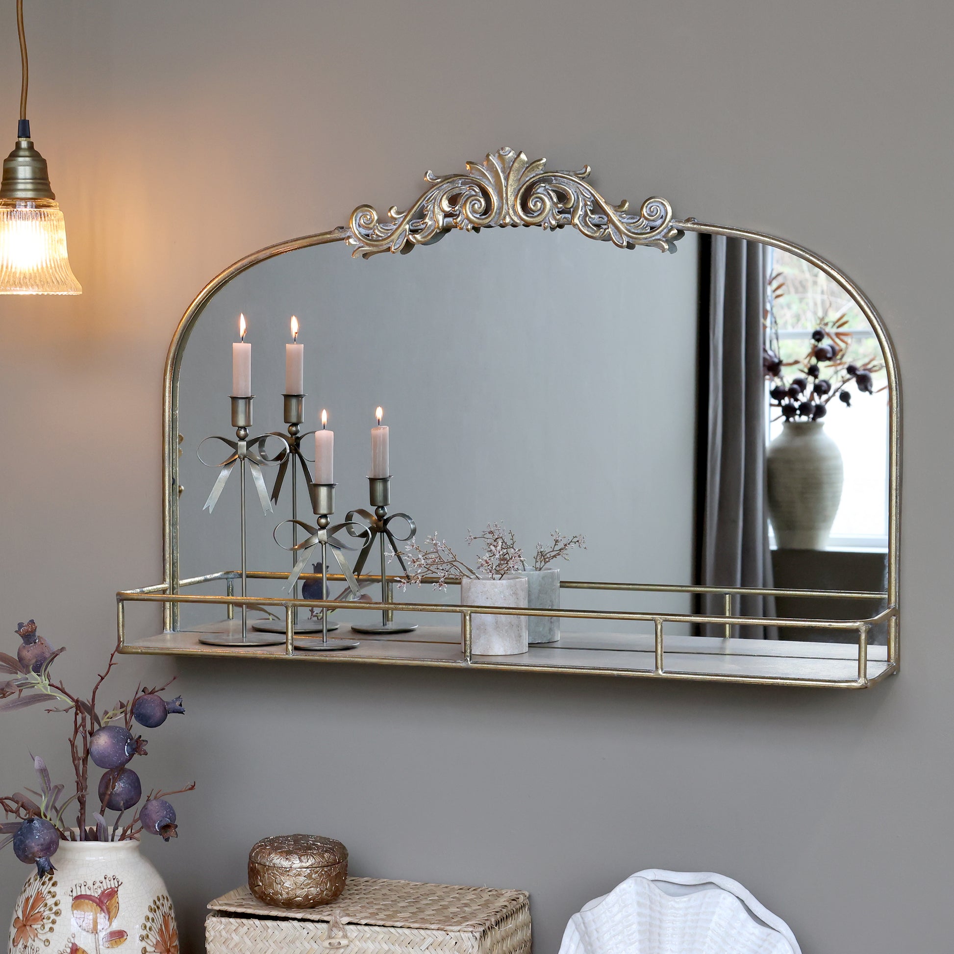 Decorative mirror with gold frame on a gray wall, with candles and decorative items.