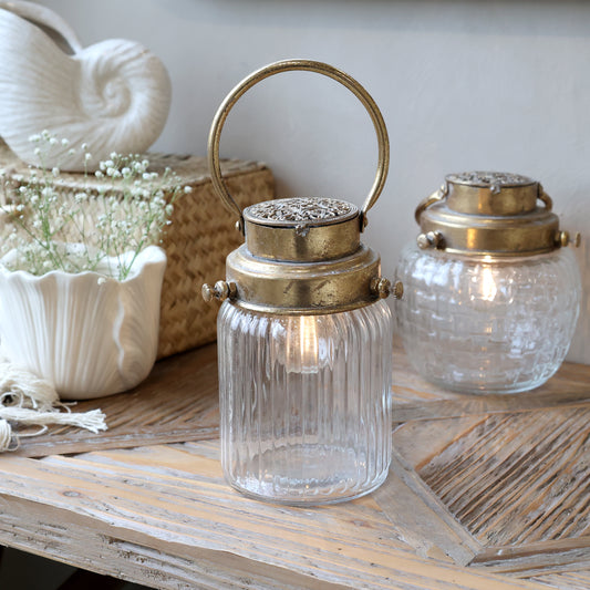 Two glass lanterns with brass lids on a wooden surface.