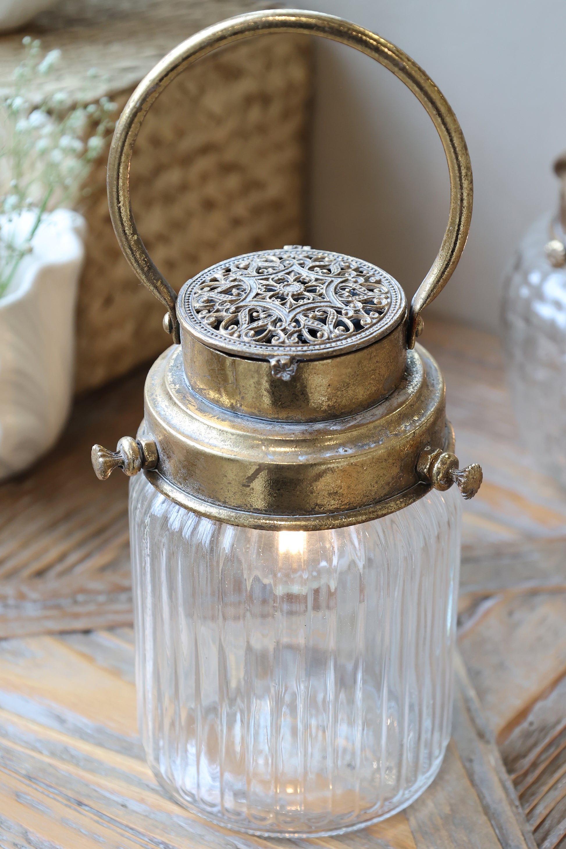Decorative lantern with glass container and ornate metal top on a wooden surface.