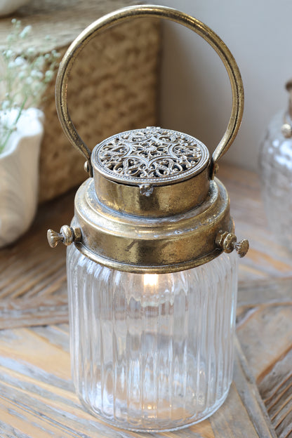 Decorative lantern with glass container and ornate metal top on a wooden surface.