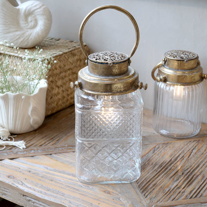 Decorative glass lanterns with metallic lids on a wooden surface.