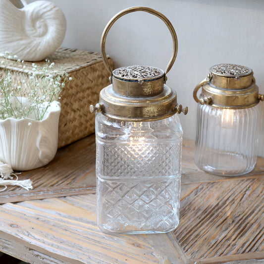 Decorative glass lanterns with metallic lids on a wooden surface.
