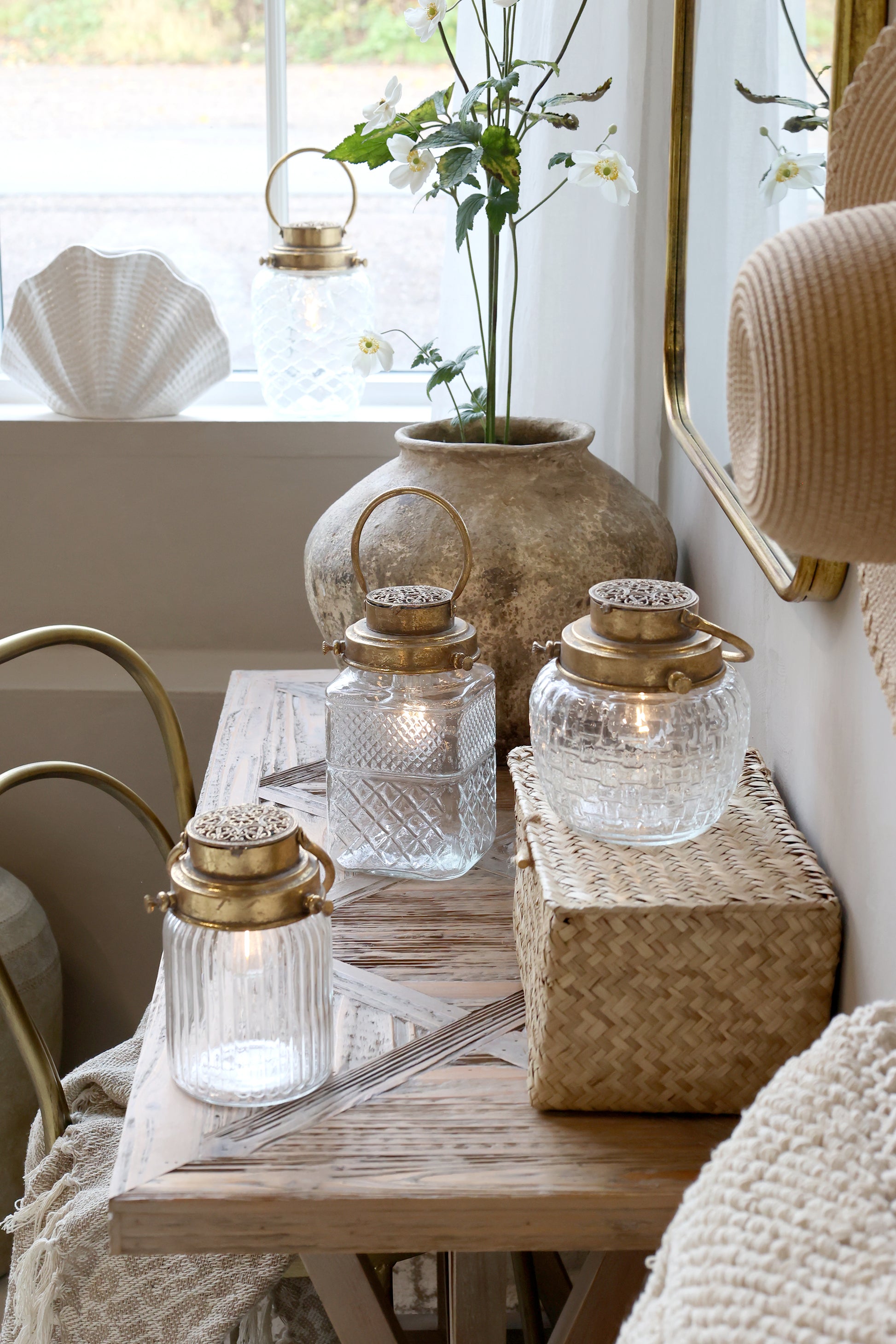 Decorative table setting with glass lanterns, a vase with flowers, and a woven basket.