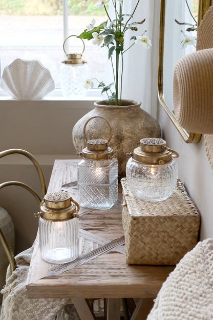 Decorative table setting with glass lanterns, a vase with flowers, and a woven basket.