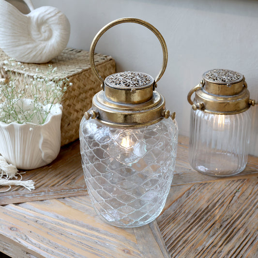 Decorative glass lanterns with gold handles on a wooden surface.