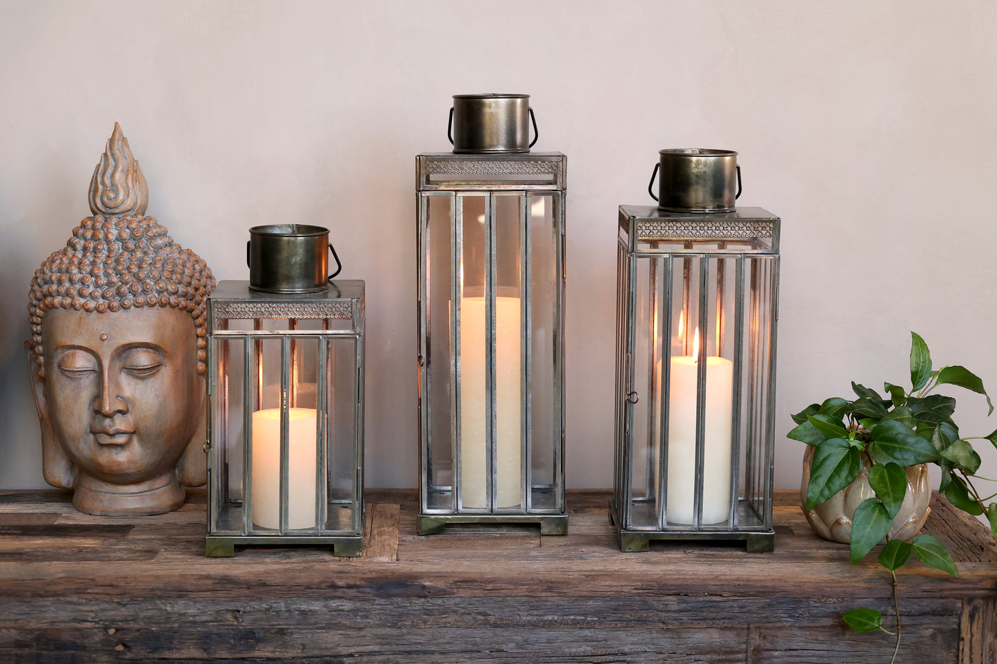 Decorative setup with Buddha statue, lanterns, and candles on a wooden surface.