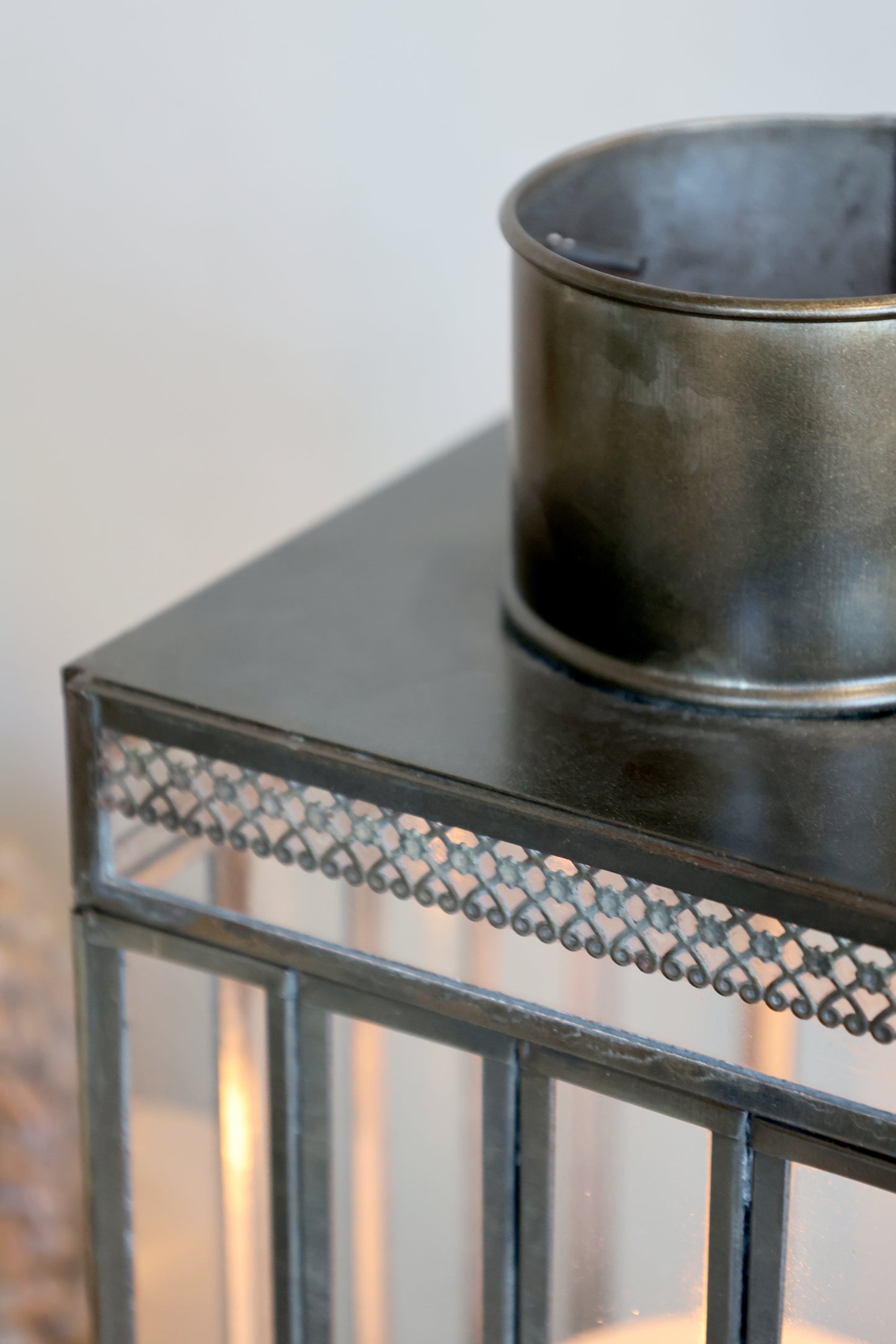 Decorative metal lantern with a dark container on top against a neutral background