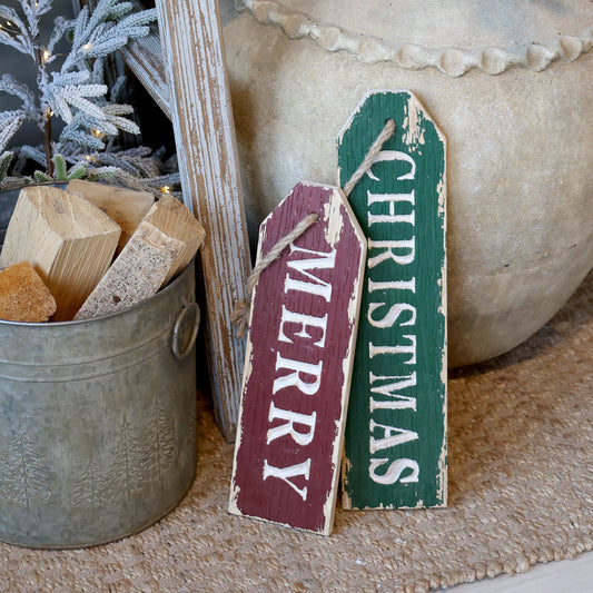 Two Christmas-themed wooden signs, one red and one green, leaning against a decorative background.