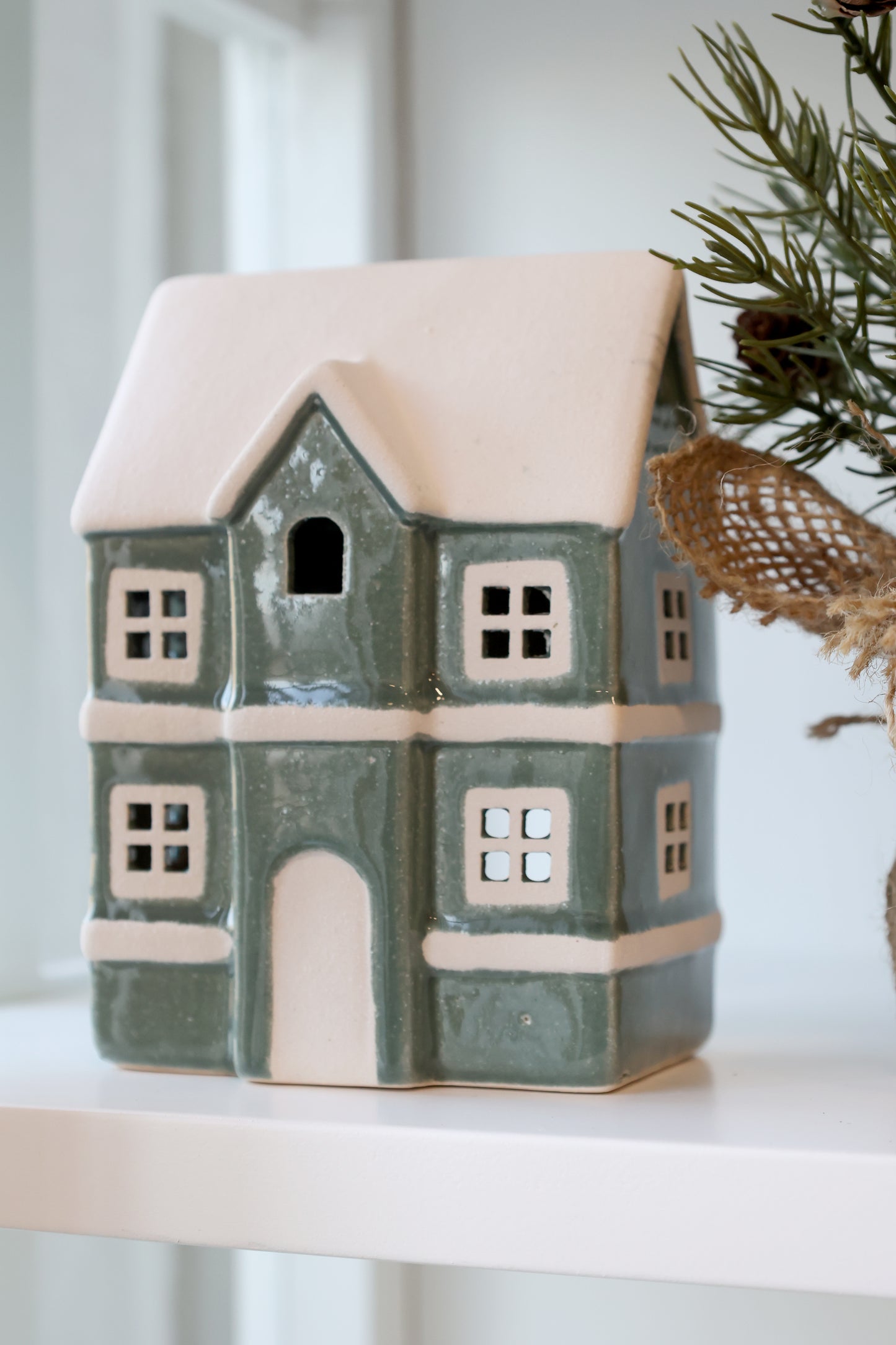 Ceramic house-shaped lantern with a snowy roof on a white surface.