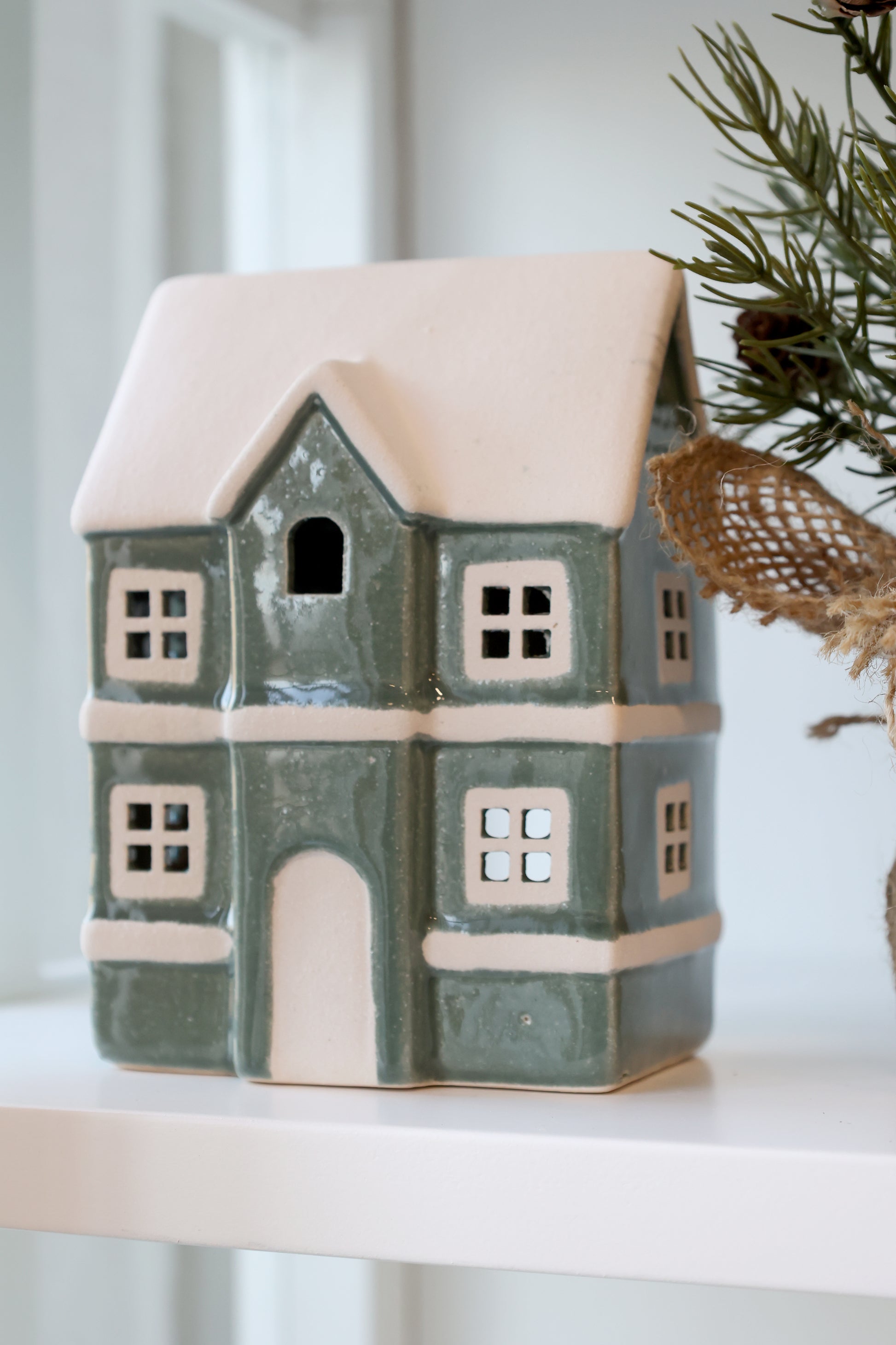Ceramic house-shaped lantern with a snowy roof on a white surface.