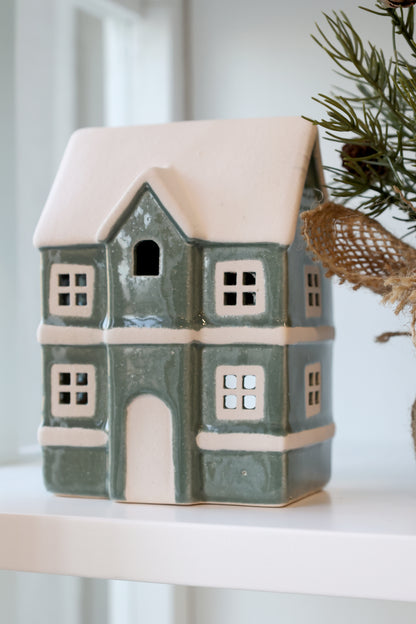 Ceramic house-shaped lantern with a snowy roof on a white surface.