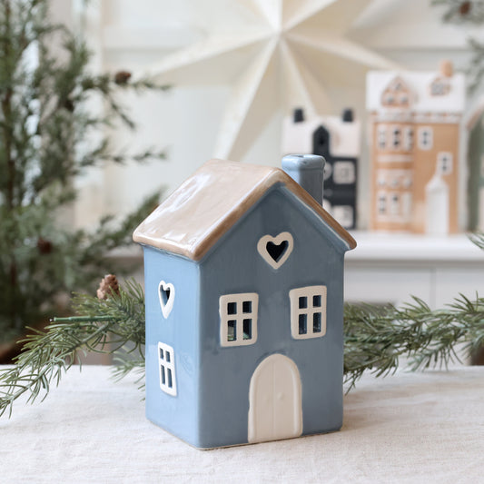 Decorative ceramic house with heart-shaped windows on a white surface with Christmas decorations in the background.