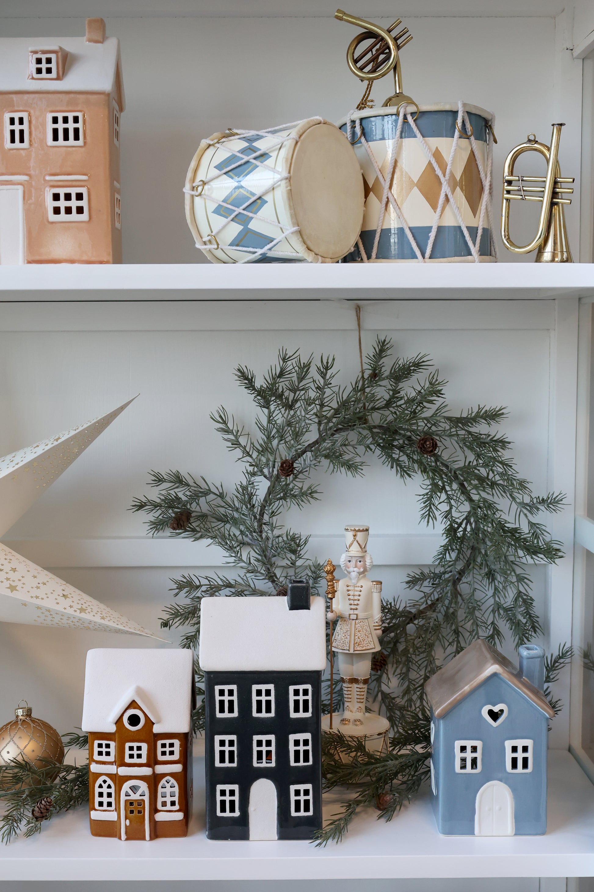 Decorative shelf with small houses, a wreath, and musical instruments on a white surface.