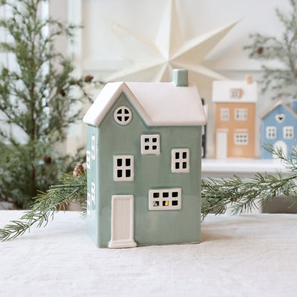 Decorative house-shaped candle holder with a snowy roof, surrounded by Christmas decorations.