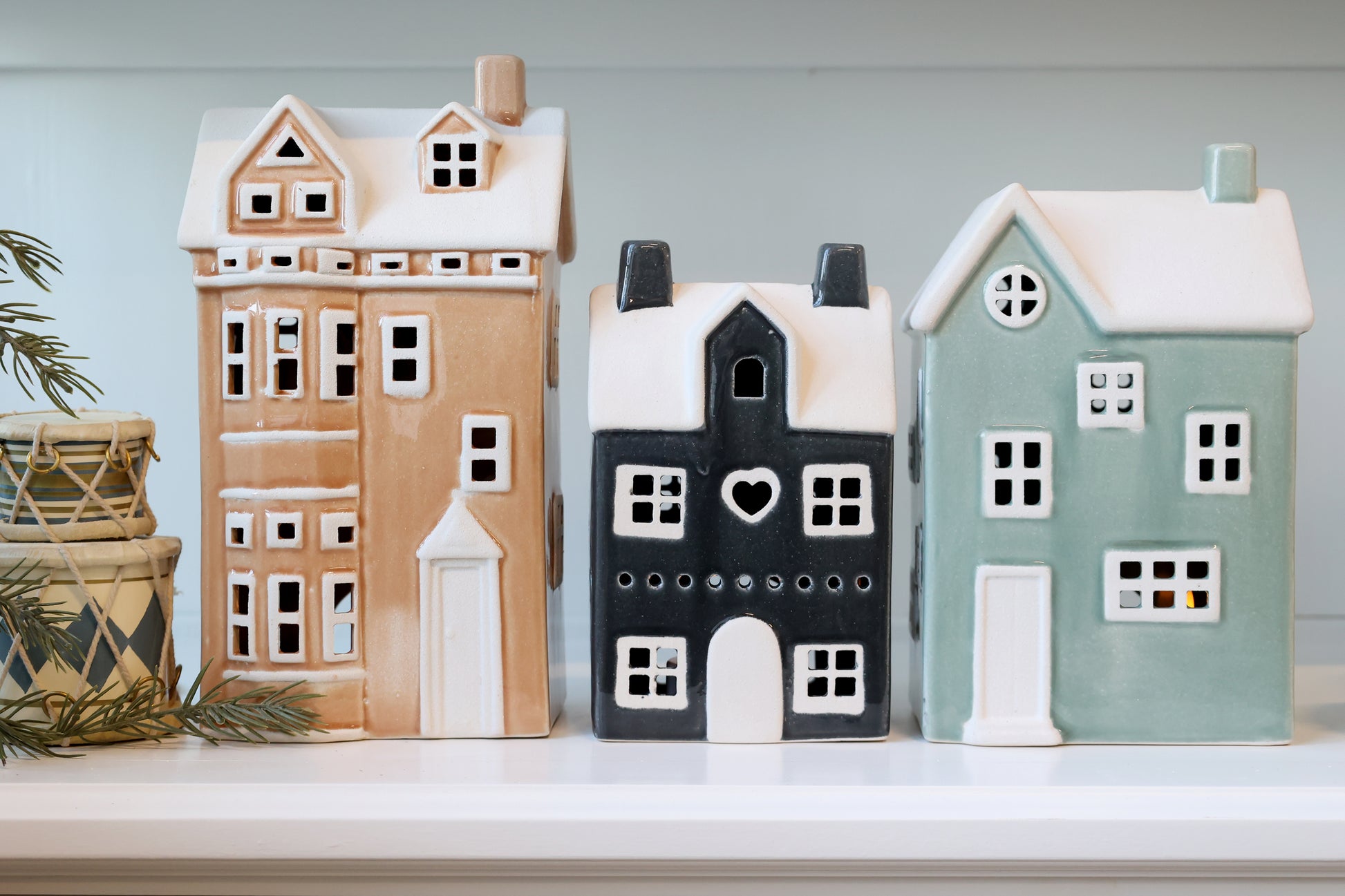 Three ceramic houses in different colors on a shelf with a light blue background