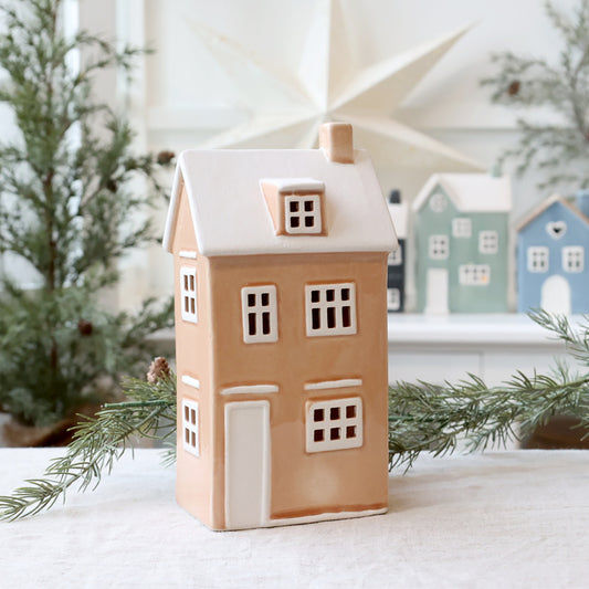 Decorative house-shaped lantern with a snowy roof, surrounded by Christmas trees and other similar houses.