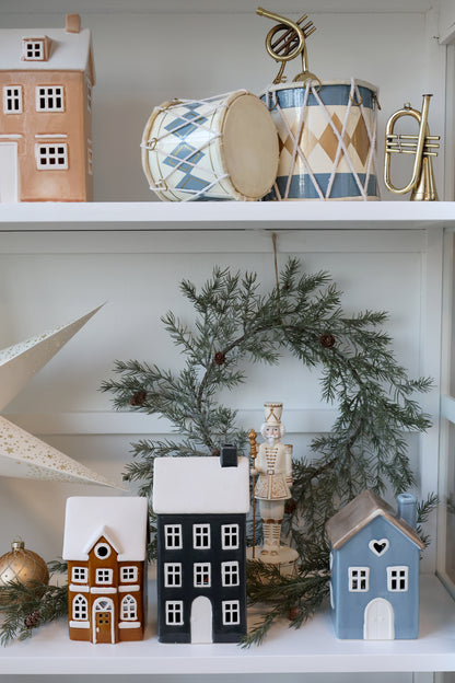 Decorative shelf with small houses, a wreath, and musical instruments on a white surface.