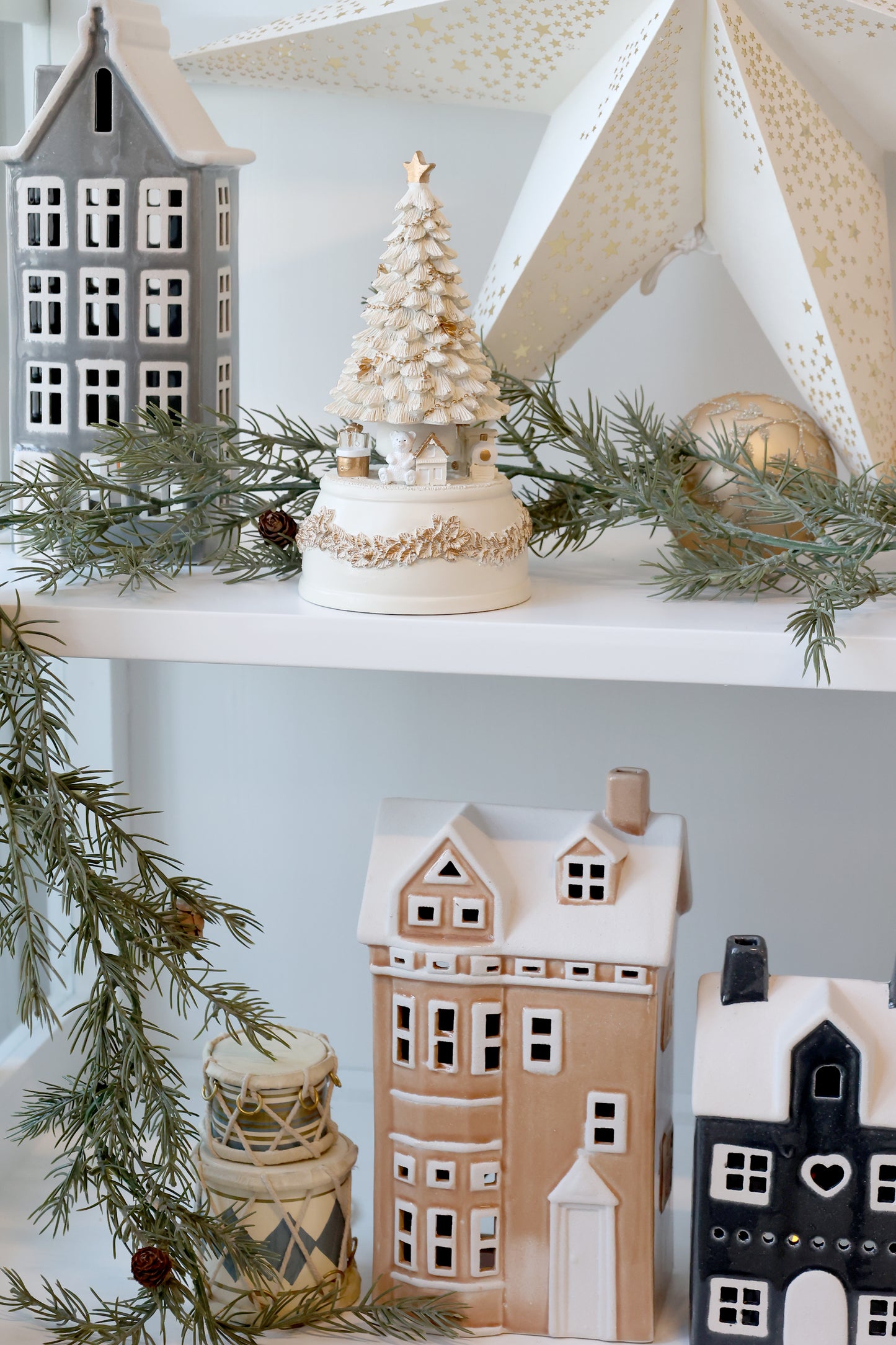 Decorative shelves with ceramic houses, a small tree, and greenery against a light blue wall.