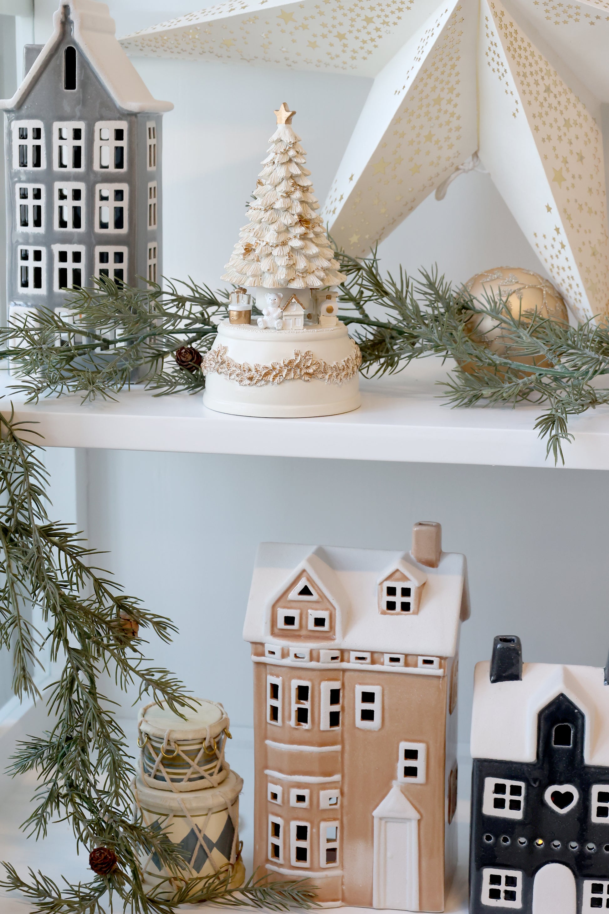 Decorative shelves with ceramic houses, a small tree, and greenery against a light blue wall.