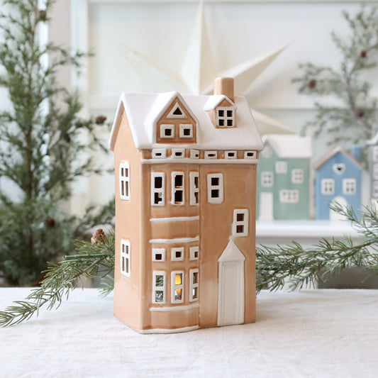 Decorative house-shaped lantern with a snowy roof, surrounded by Christmas trees.