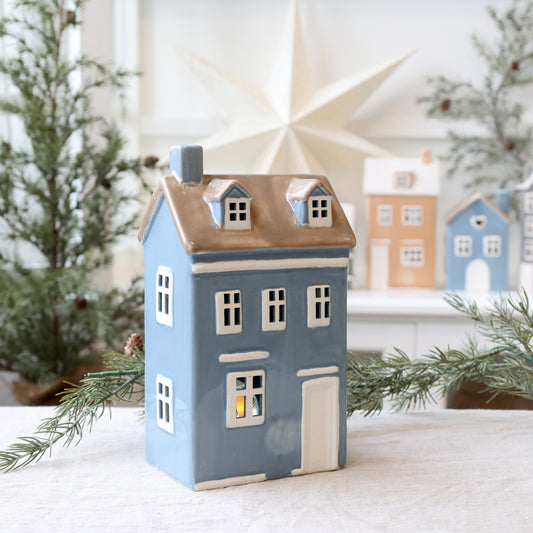 Decorative house-shaped lantern with a warm glow, surrounded by Christmas trees.