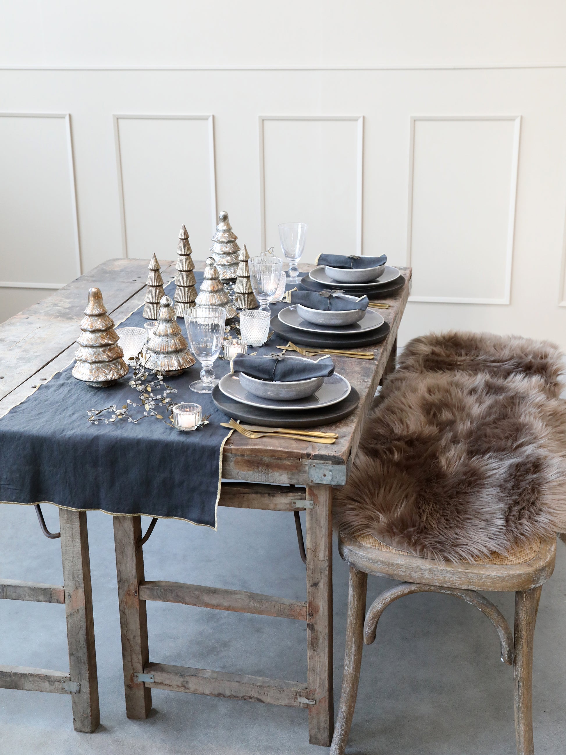 Dining table set with gray tablecloth, plates, and decorative items in a room with white paneled walls.