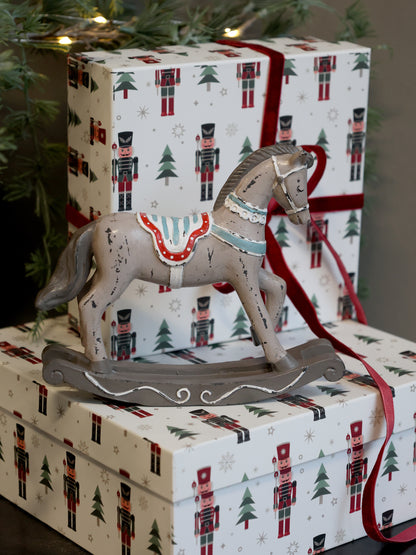 Decorative rocking horse on a wrapped gift with Christmas-themed wrapping paper.
