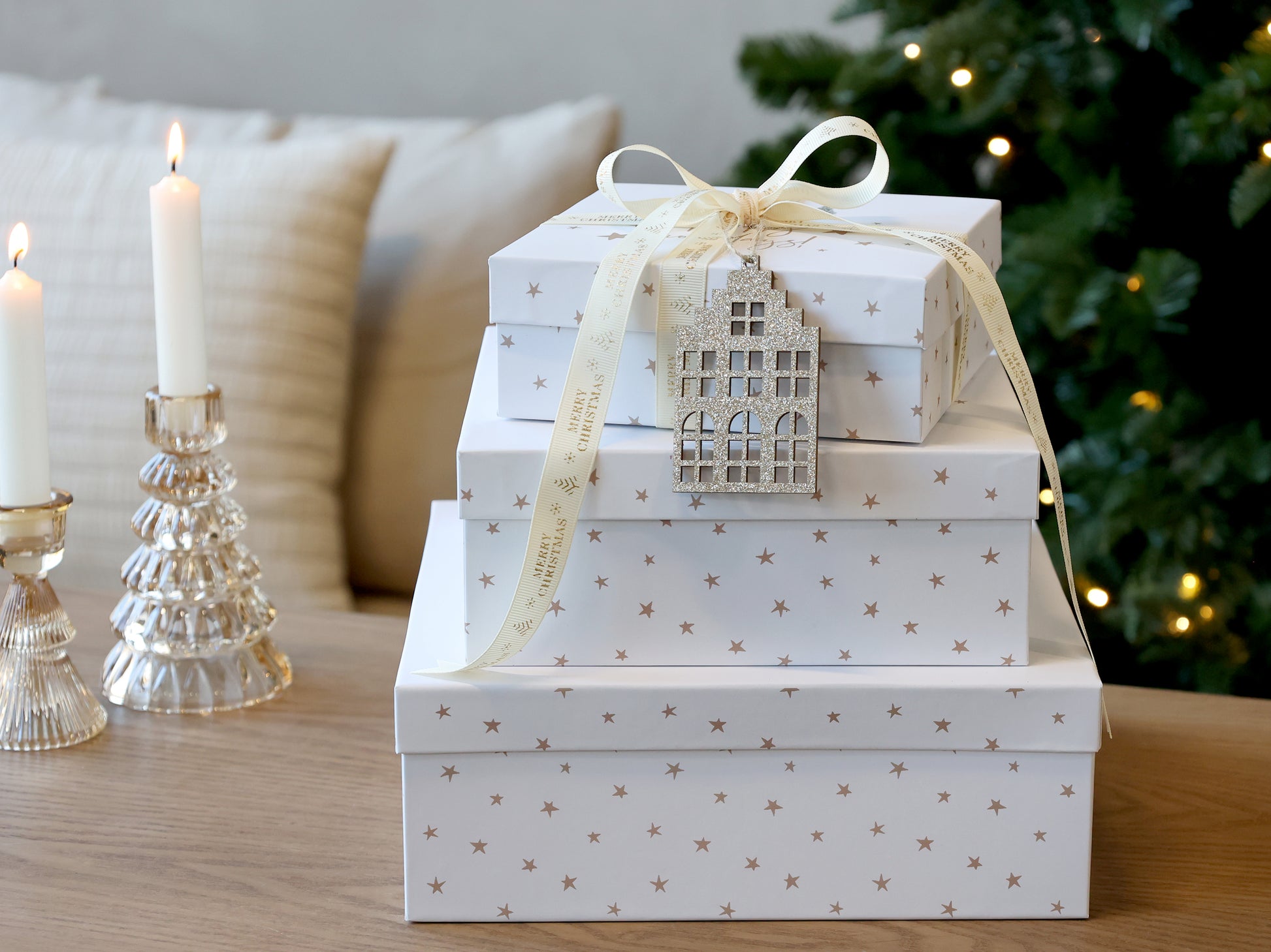 Stack of white gift boxes with star patterns on a wooden surface, Christmas tree in the background