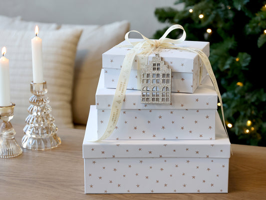 Stack of white gift boxes with star patterns on a wooden surface, Christmas tree in the background