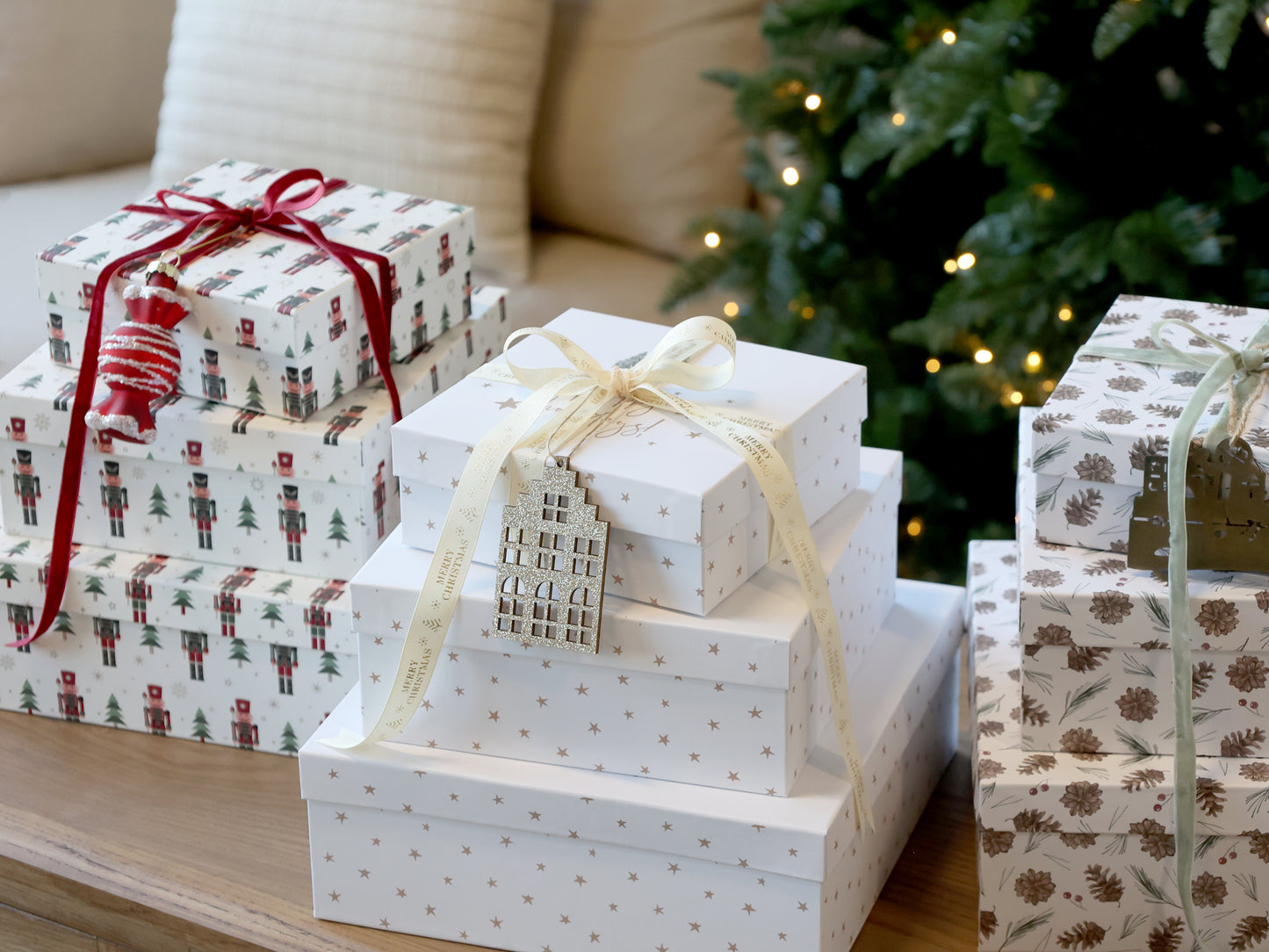 Stack of Christmas presents with decorative ribbons on a table in front of a decorated tree.