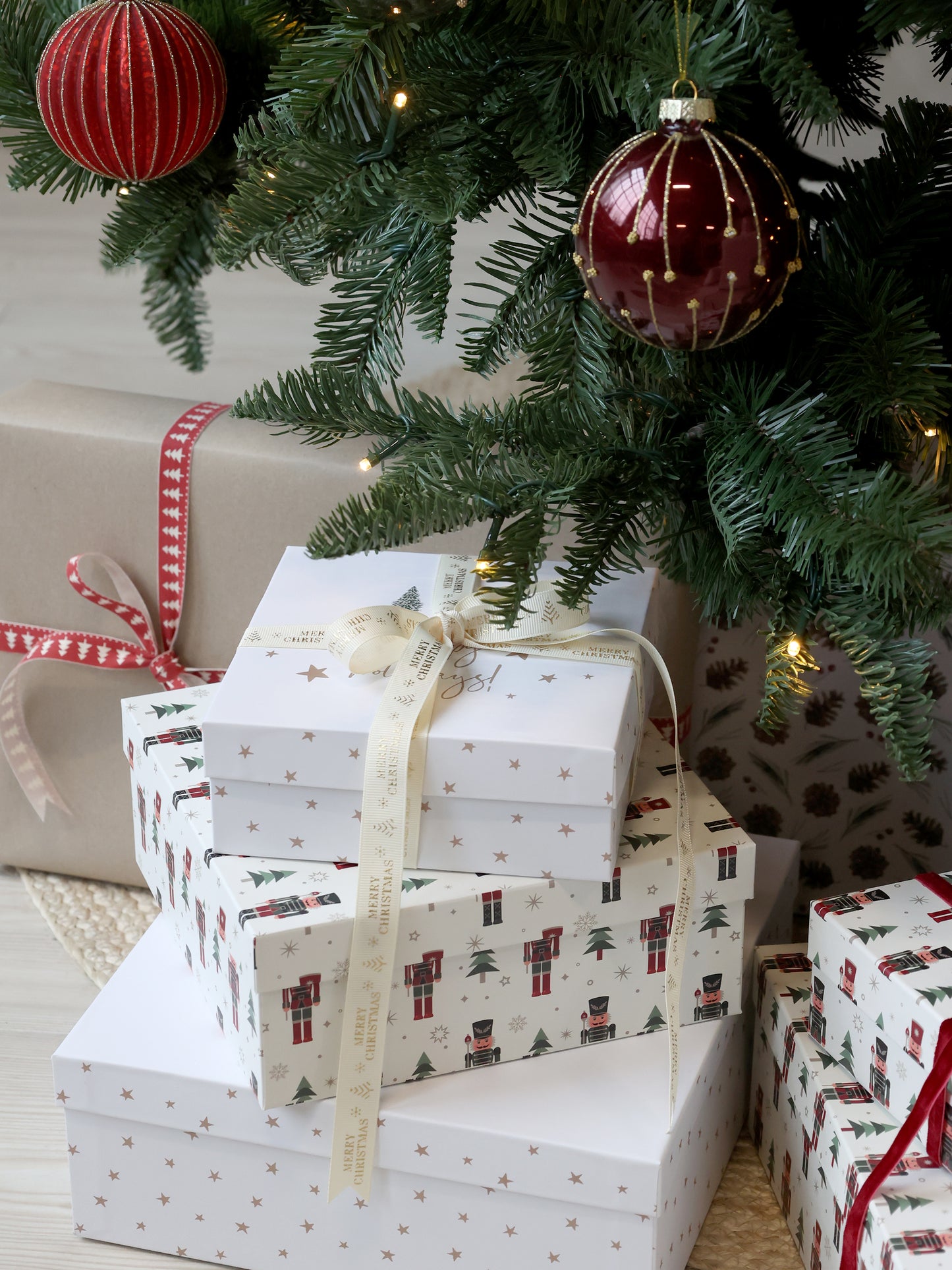 Stack of Christmas presents under a decorated tree with red ornaments.